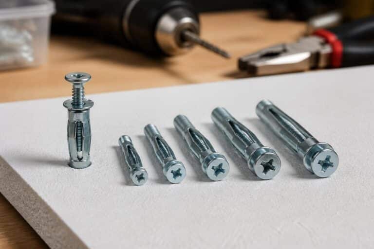 Six chevilles métalliques de tailles différentes posées sur une plaque de plâtre